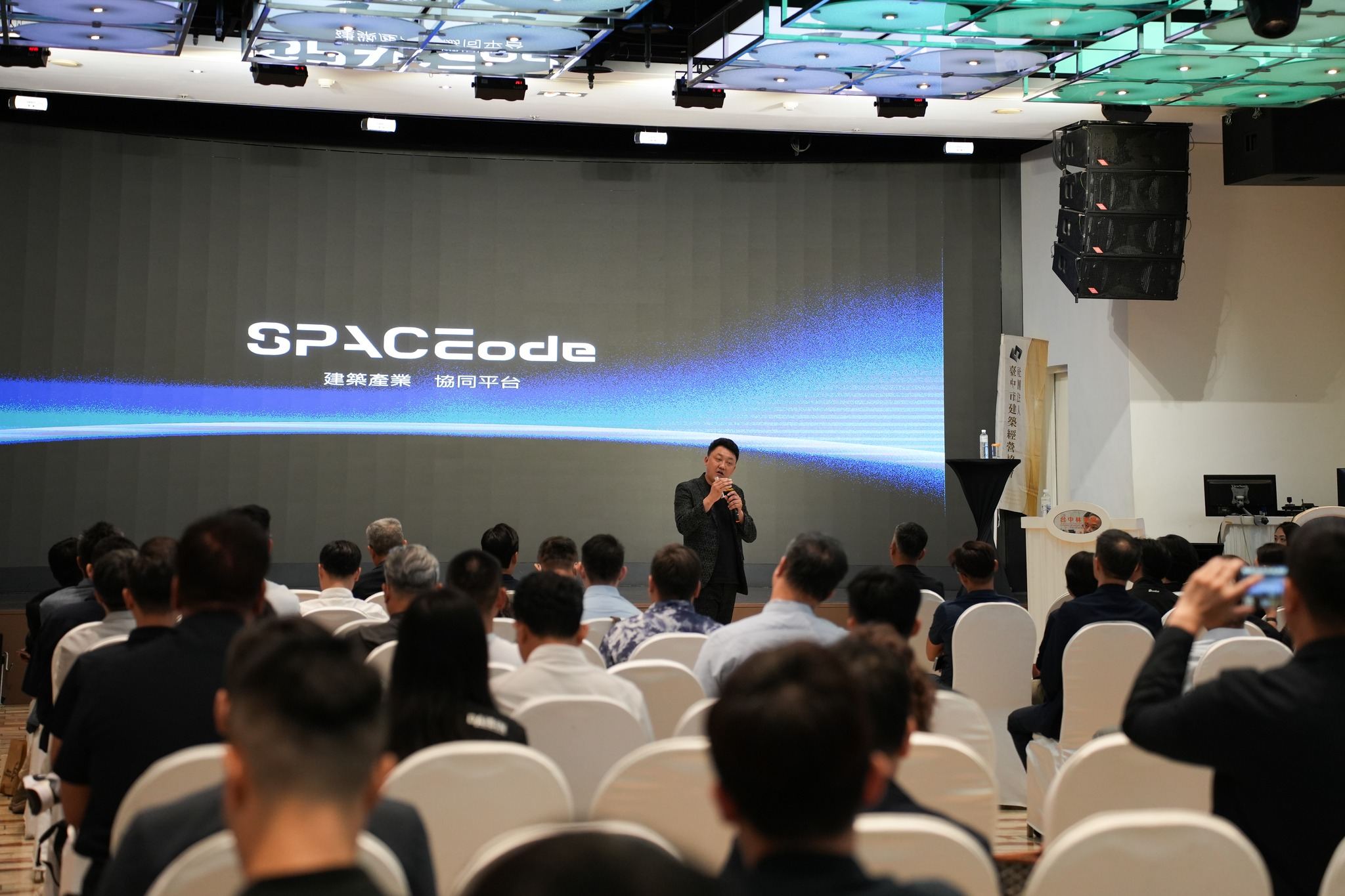 臺中市建築經營協會大師講座現場,講者在顯示「SPACEcode 建築產業協同平台」的大型 LED 螢幕前分享,台下座無虛席